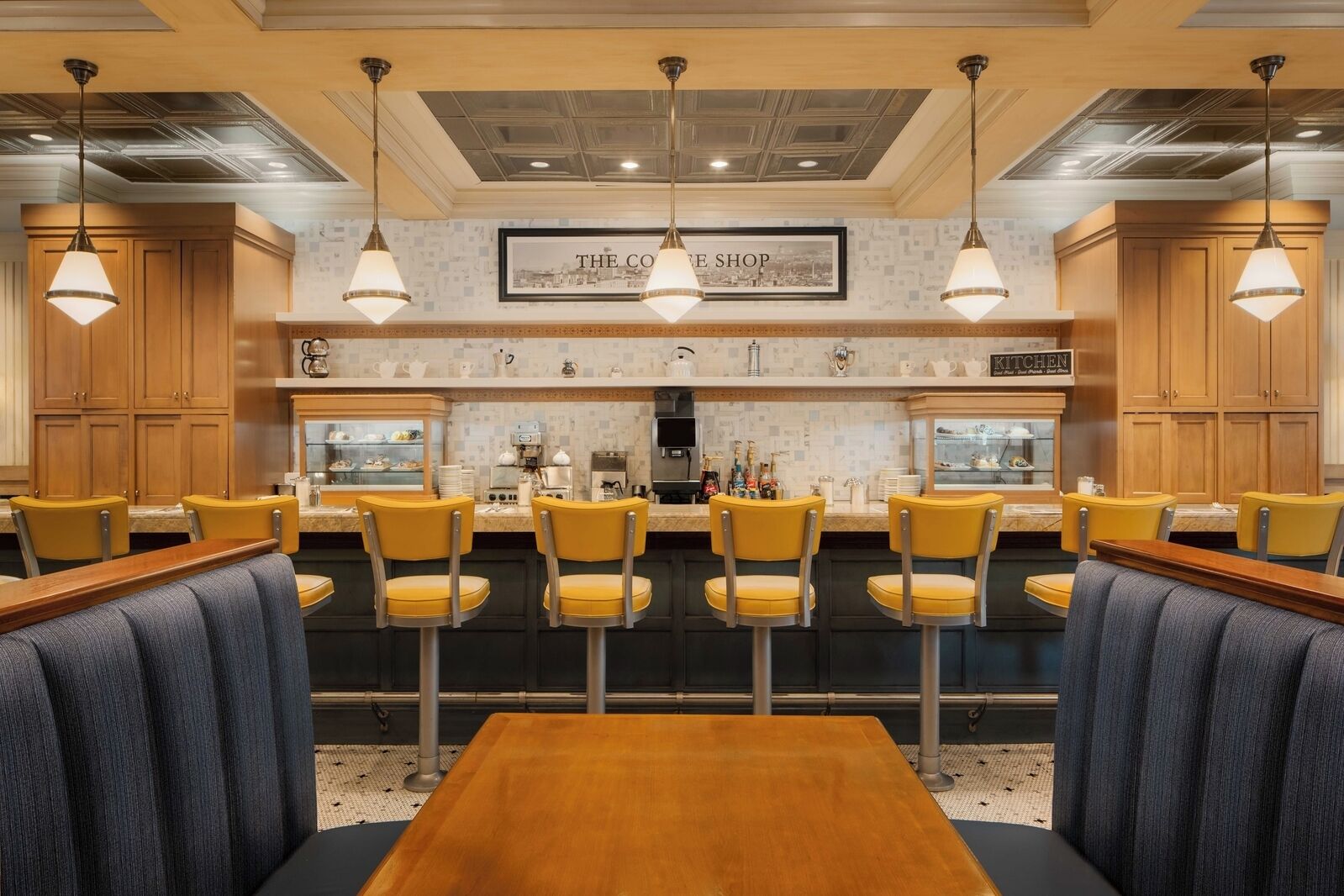 Un restaurante con zona de bar, sillas amarillas y una mesa de madera.