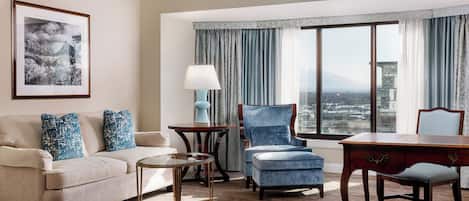 Habitación de hotel con un ventanal grande, un sofá, una silla, una mesa y una lámpara.