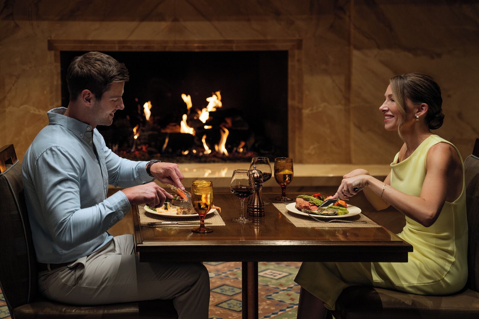 A couple dining at a table with a fireplace in the background.