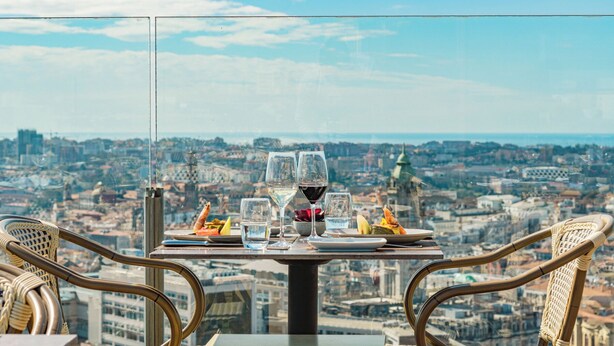 A table with two glasses of wine, a plate of food, and a glass of water, set against a cityscape view. - Hotel Dom Henrique Downtown (Porto)