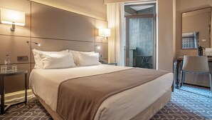 A hotel room with a large bed, bedside lamps, a small table with a bottle and glasses, a chair, and a view of a balcony. - Hotel Dom Henrique Downtown (Porto)