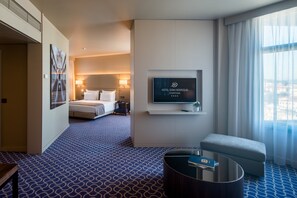 Une chambre d’hôtel avec un lit, un téléviseur fixé au mur, une petite table et une fenêtre avec des rideaux.