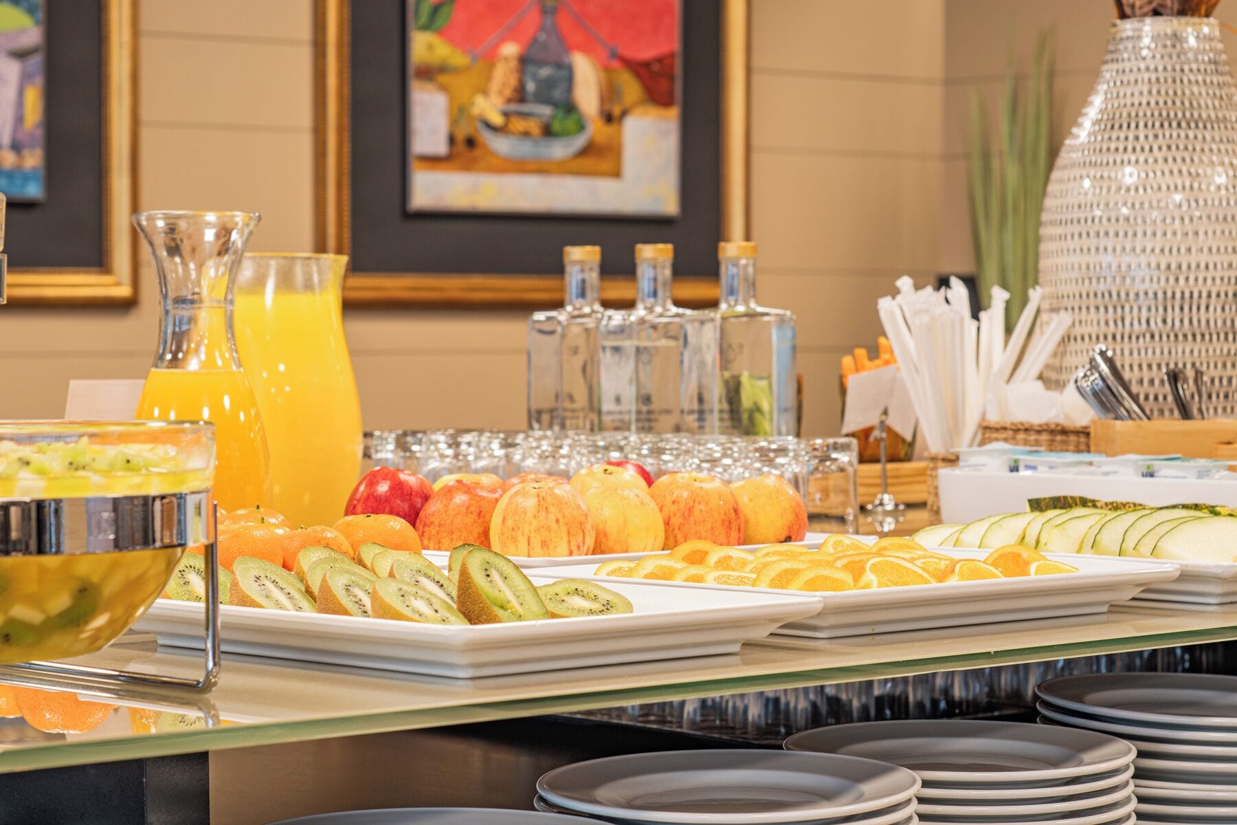 A buffet with various fruits, a glass of orange juice, and several bottles of water.