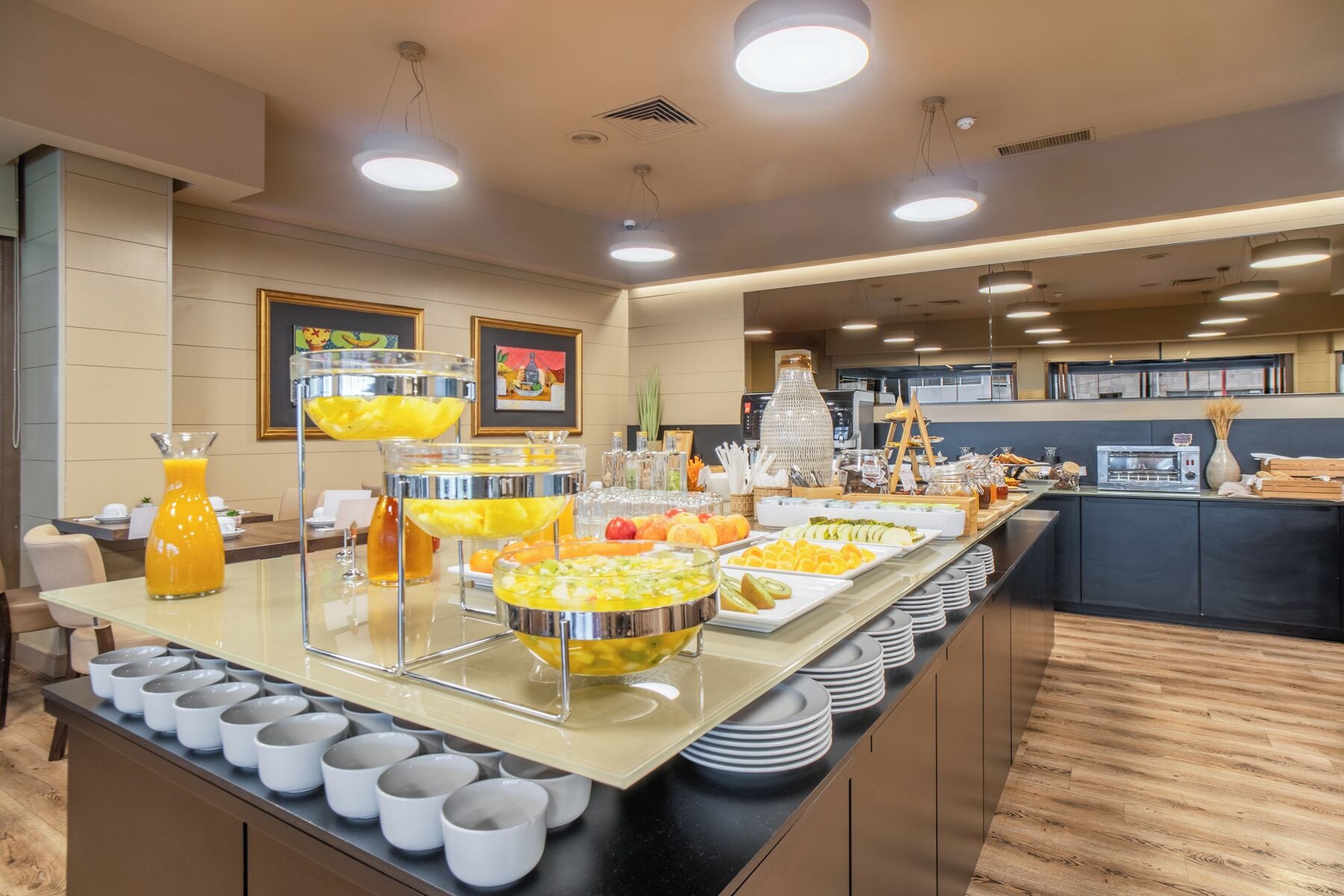 Una barra de buffet con diversos alimentos y bebidas, incluyendo cuencos de fruta y un dispensador de jugo.