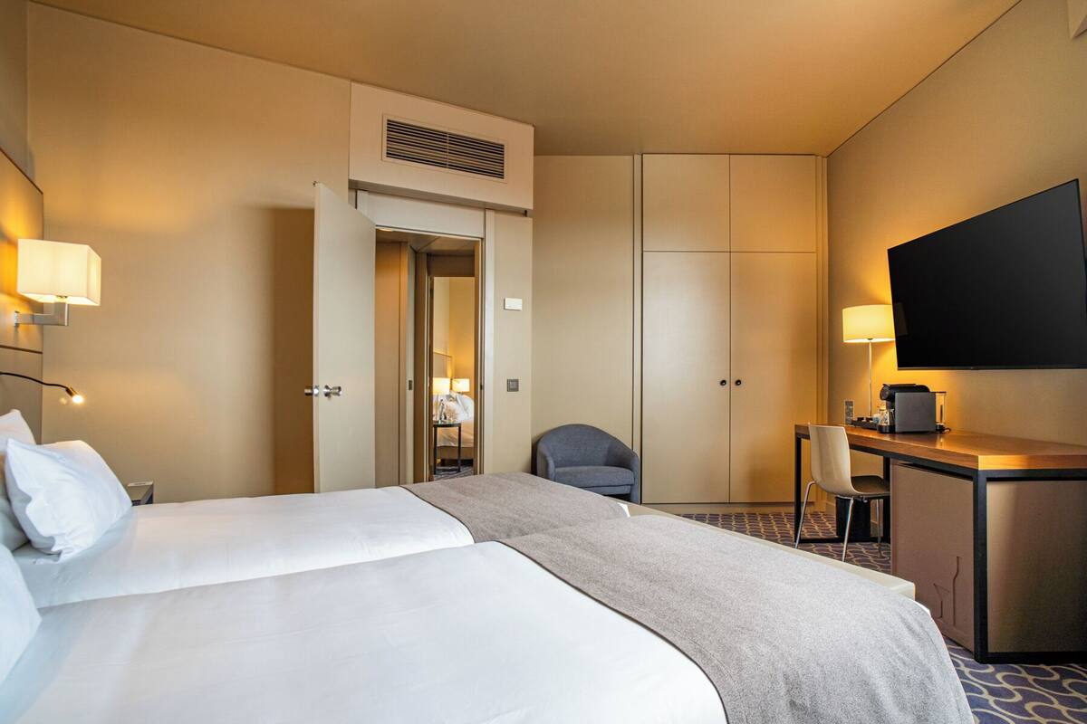 A hotel room with a bed, a desk, a chair, a television, and a door leading to a bathroom.