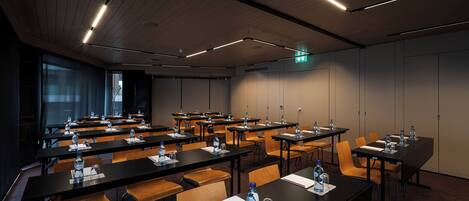 A conference room with multiple tables, chairs, water bottles, and a projector screen.
