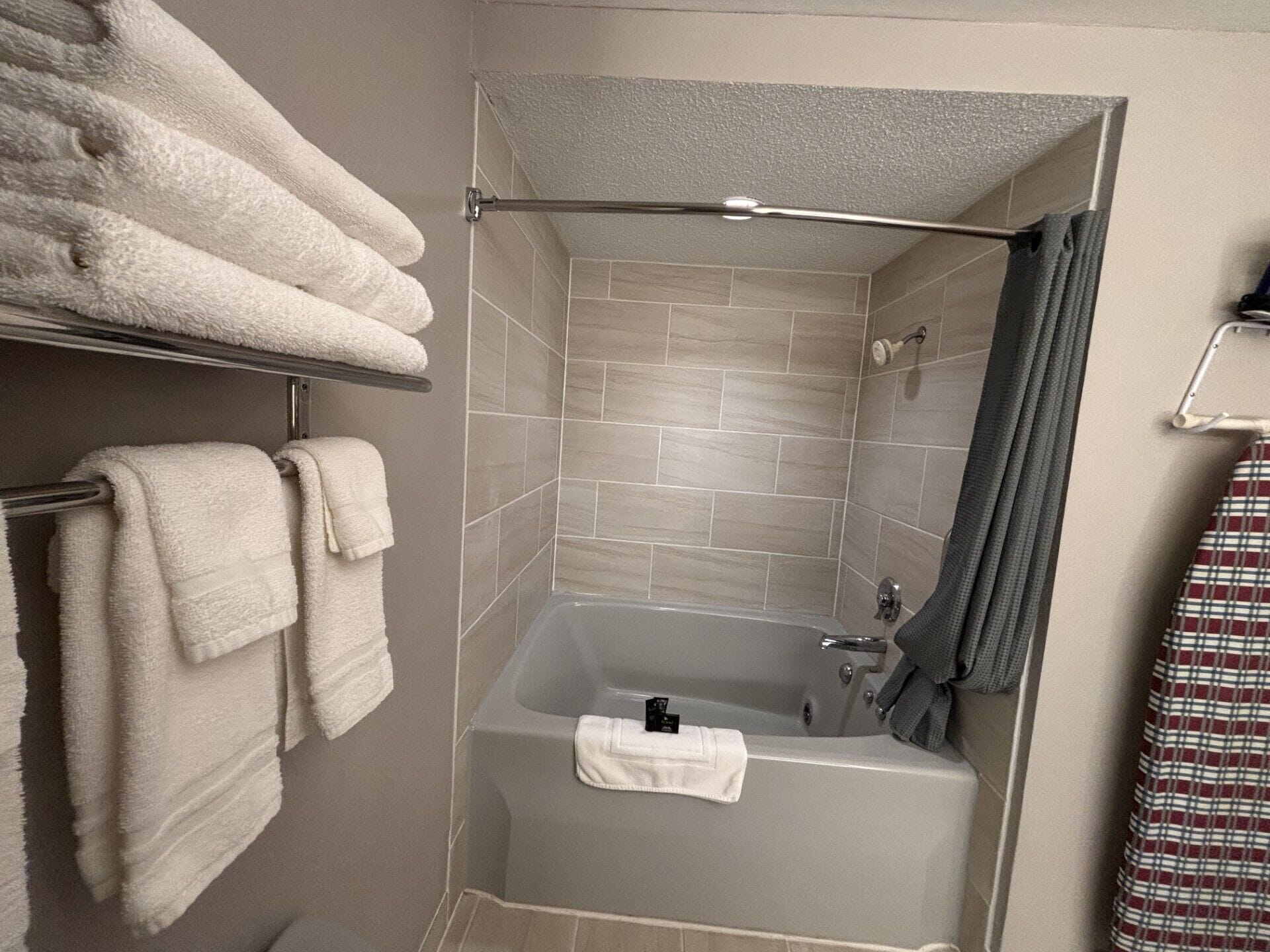 A bathroom with a bathtub, a towel rack with multiple towels, and a shower curtain.