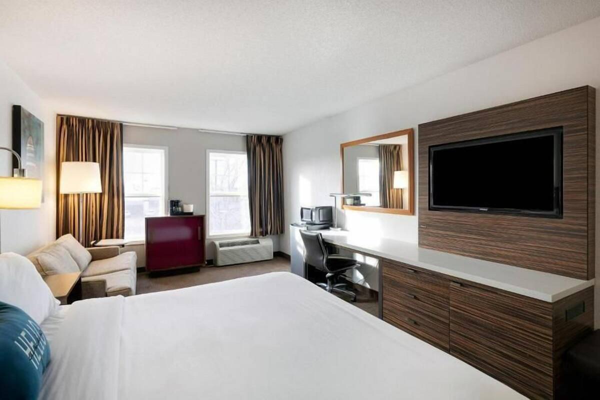 A hotel room with a large bed, a desk with a computer, a TV, a red dresser, and a window with curtains.