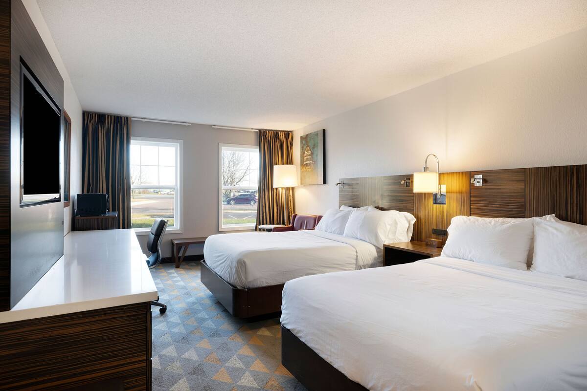 A hotel room with two beds, a desk, a chair, a TV, and a window with curtains.