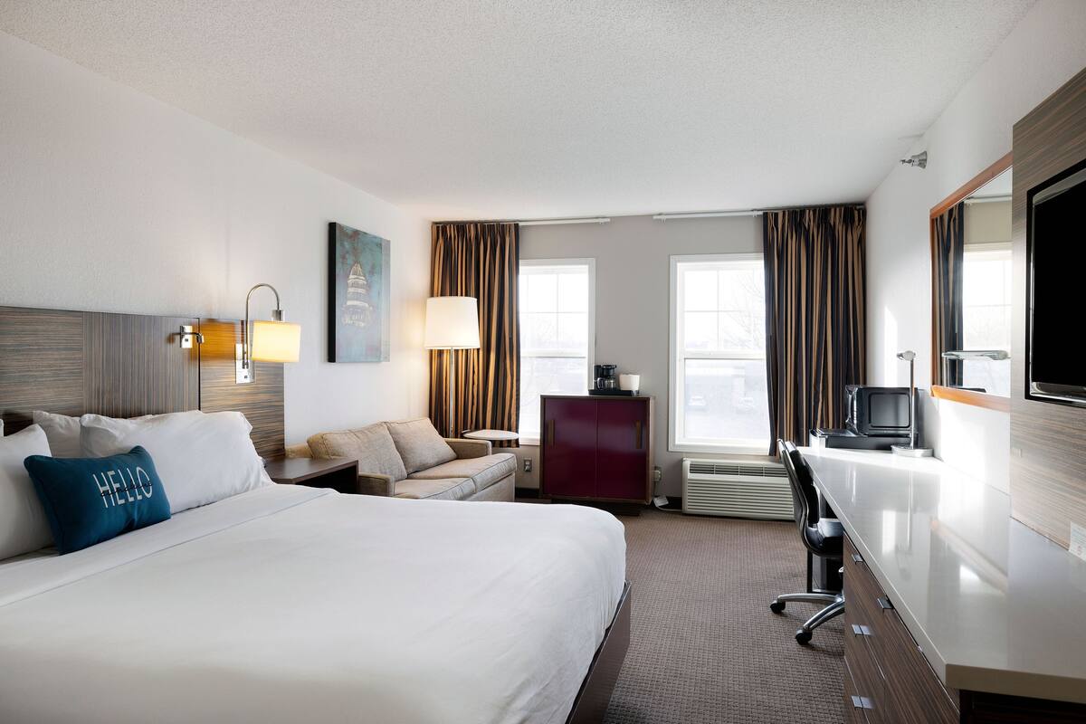 A hotel room with a large bed, a desk, a chair, a television, and a window with curtains.
