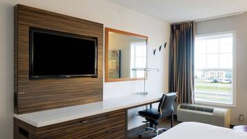 Habitación de hotel con televisor de pantalla plana grande, escritorio con silla, cama, ventana con cortinas y vistas al exterior.