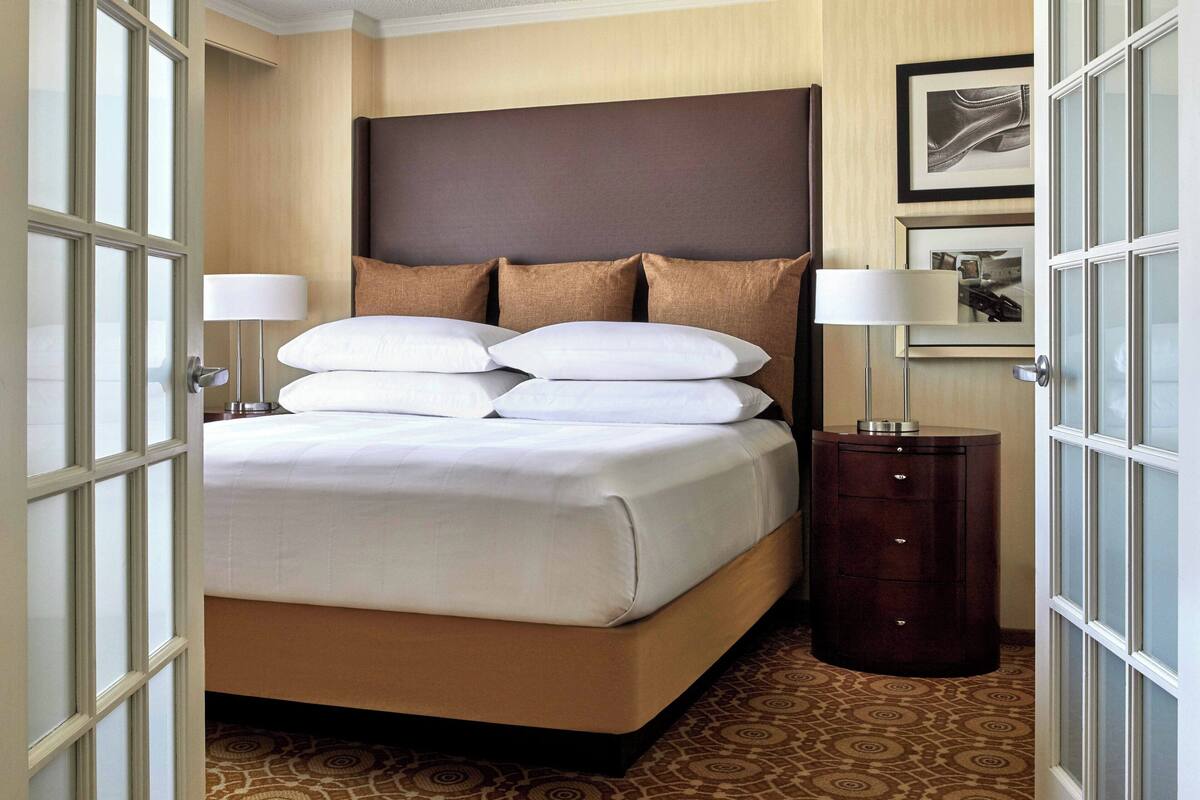 Quarto de hotel com uma cama grande, uma mesa de cabeceira e uma luminária fixada na parede.