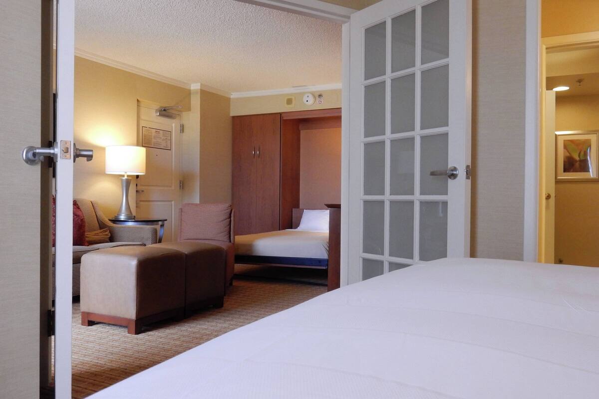 Quarto de hotel com uma cama, uma escrivaninha com luminária, uma cadeira e um guarda-roupa.