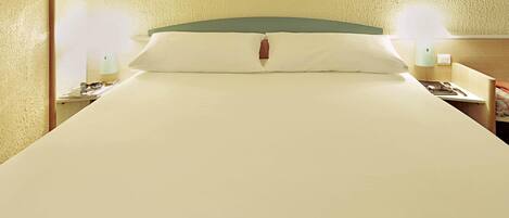 Una cama bien tendida con un cabecero verde, dos lámparas de noche y una mesita de noche con lámpara y teléfono.