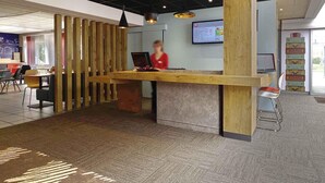 A reception desk with a wooden panel design, a computer, and a digital display. - ibis Poitiers Beaulieu (Poitiers)