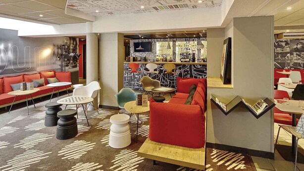 A modern lounge area with red sofas, white chairs, and a bar area with a patterned wall. - ibis Poitiers Beaulieu (Poitiers)