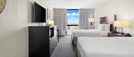 A hotel room with two beds, a TV, a desk, and a window with a view.