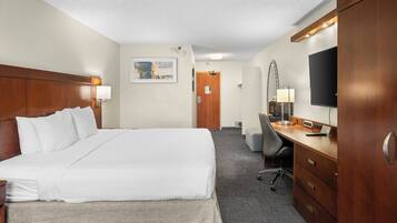 Quarto de hotel com cama grande, uma escrivaninha, uma cadeira, televisão e guarda-roupa.