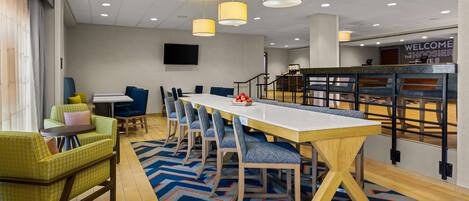 A modern conference room with a long table, blue and yellow chairs, and a 'Welcome to the Hoosier State' sign.