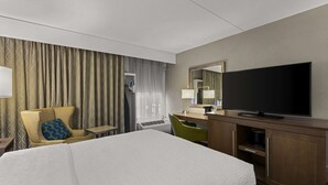 A hotel room with a large bed, a desk with a flat-screen TV, a chair, a desk lamp, and a mirror. - Hampton Inn Bloomington (Bloomington)