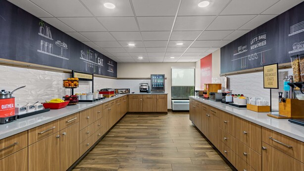 A modern kitchen with wooden cabinets, a central island, and a chalkboard wall with food-related drawings. - Hampton Inn Bloomington (Bloomington)