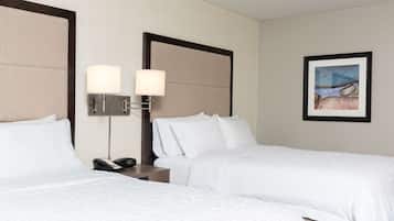 Habitación de hotel con dos camas, una mesita de noche con lámpara, teléfono y un cuadro en la pared.