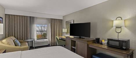 Ein Hotelzimmer mit einem Bett, einem Schreibtisch mit Fernseher, einer Mikrowelle und einem Fenster mit Vorhängen.