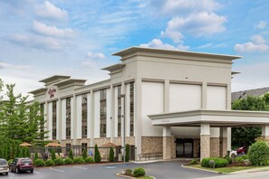 A modern hotel with a large entrance, a covered parking area, and a landscaped front yard.