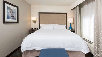 A hotel room with a large bed, a bedside table with a lamp, a framed picture on the wall, and a window with curtains.