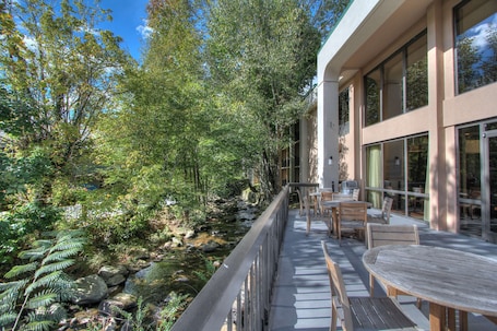 A deck with outdoor seating overlooking a stream and dense foliage.
