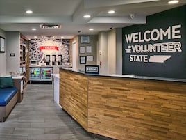 Un área de recepción con un mostrador de madera, un cartel que dice 'Welcome the Volunteer State', un cartel con la palabra 'Pantry' y una pared con una máquina de café y un cartel que dice 'Treats'.