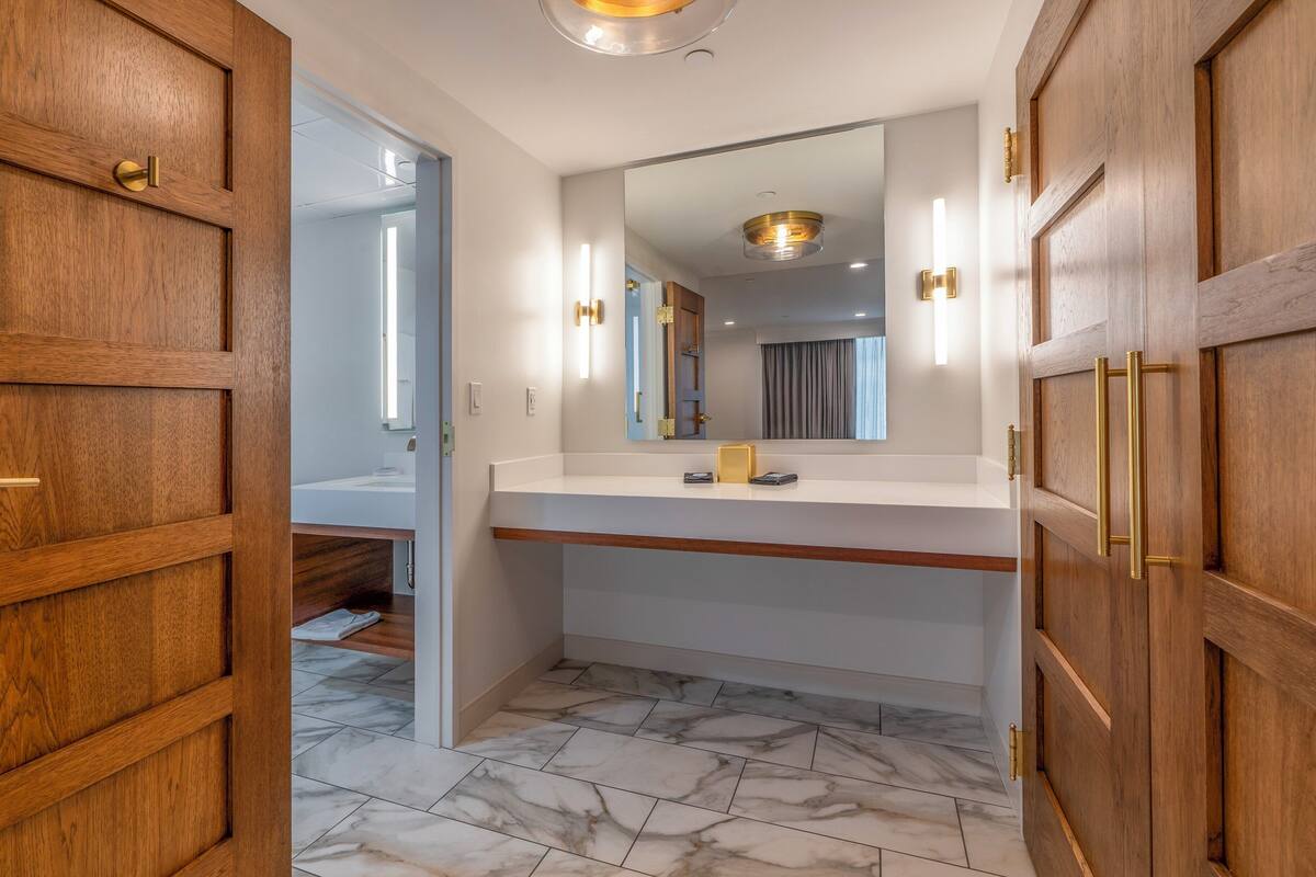 A modern bathroom with wooden doors, a marble floor, and a white vanity with a mirror.