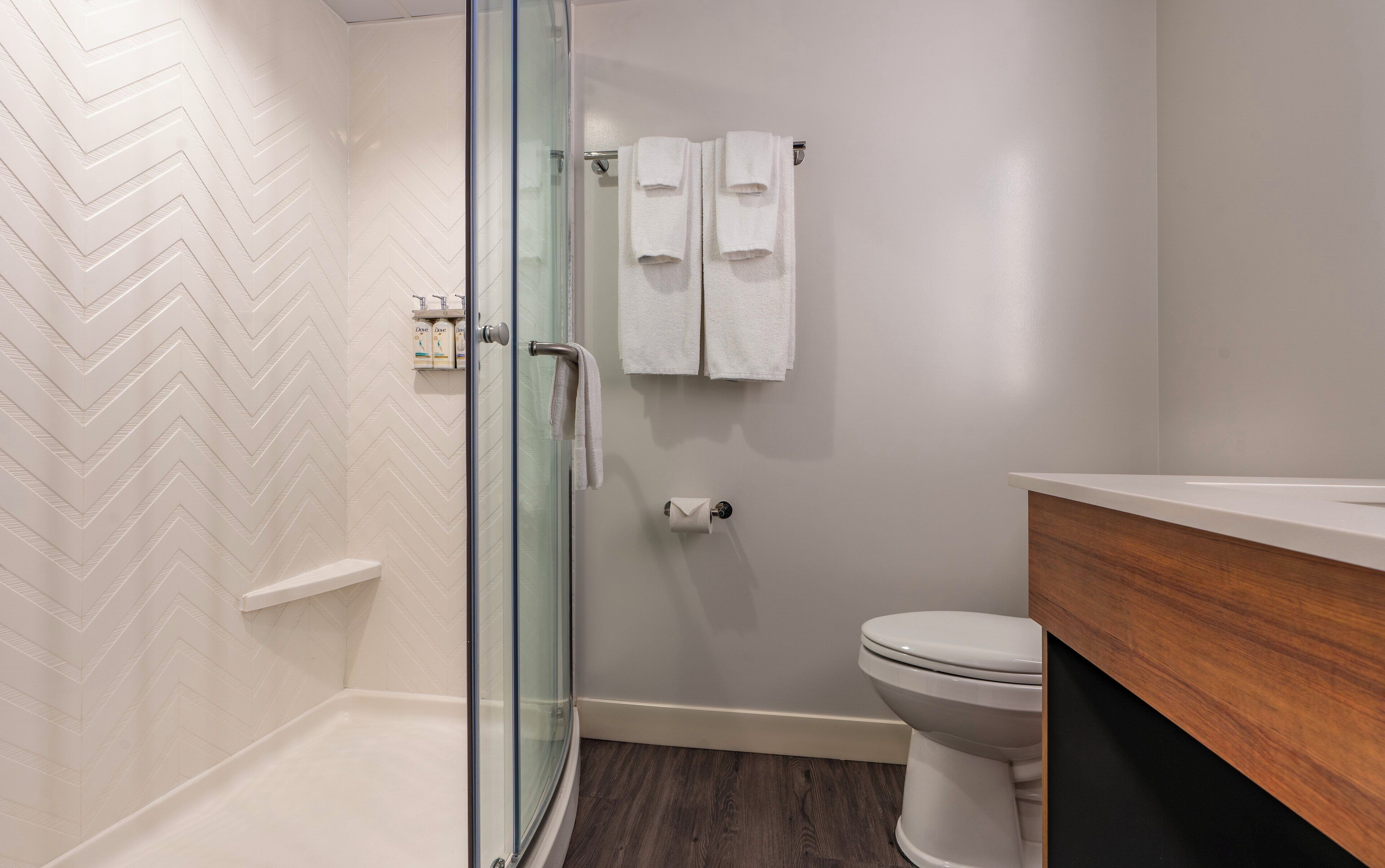 Un baño moderno con cabina de ducha de vidrio, inodoro y tocador de madera.