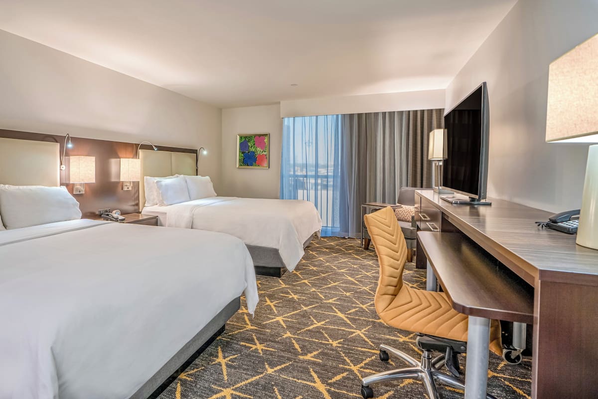 A hotel room with two beds, a desk with a chair, a television, and a window with curtains.