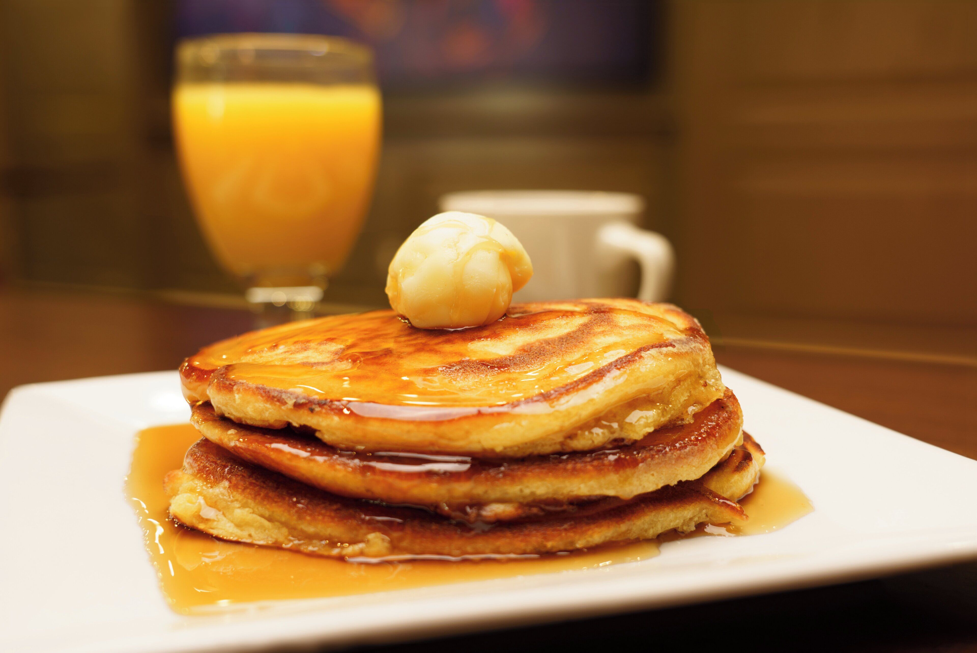 Une pile de crêpes arrosées de sirop, avec une noisette de beurre sur le dessus, servies dans une assiette blanche.