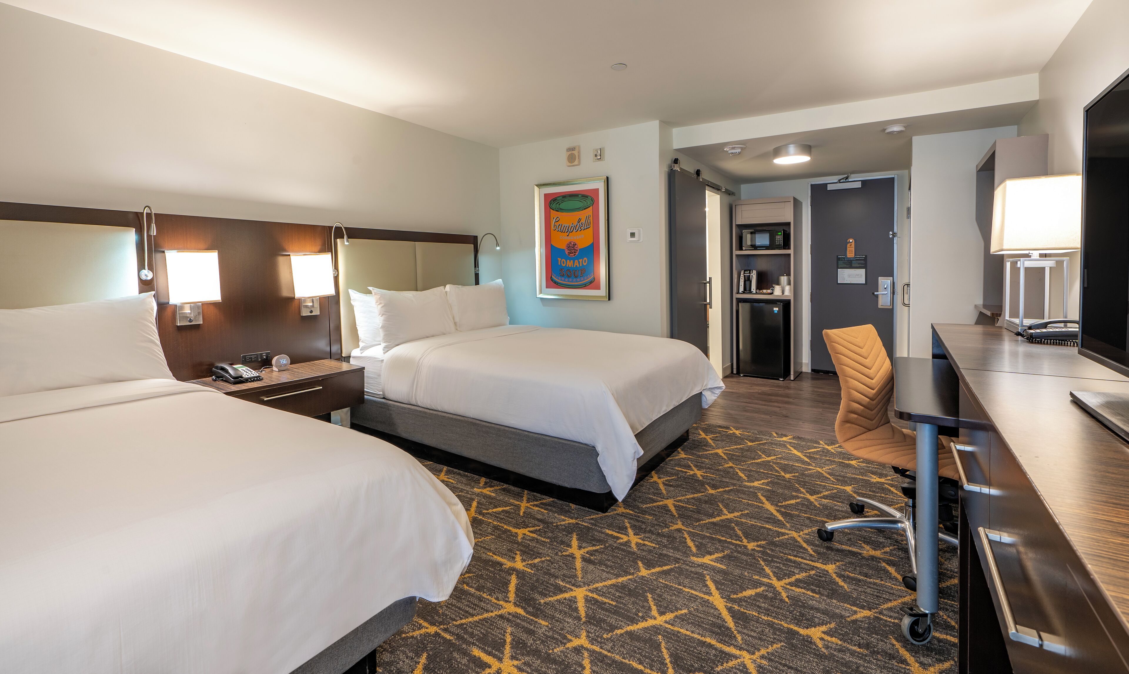 Une chambre d’hôtel avec deux lits, un bureau avec une lampe, un four à micro-ondes et un réfrigérateur.