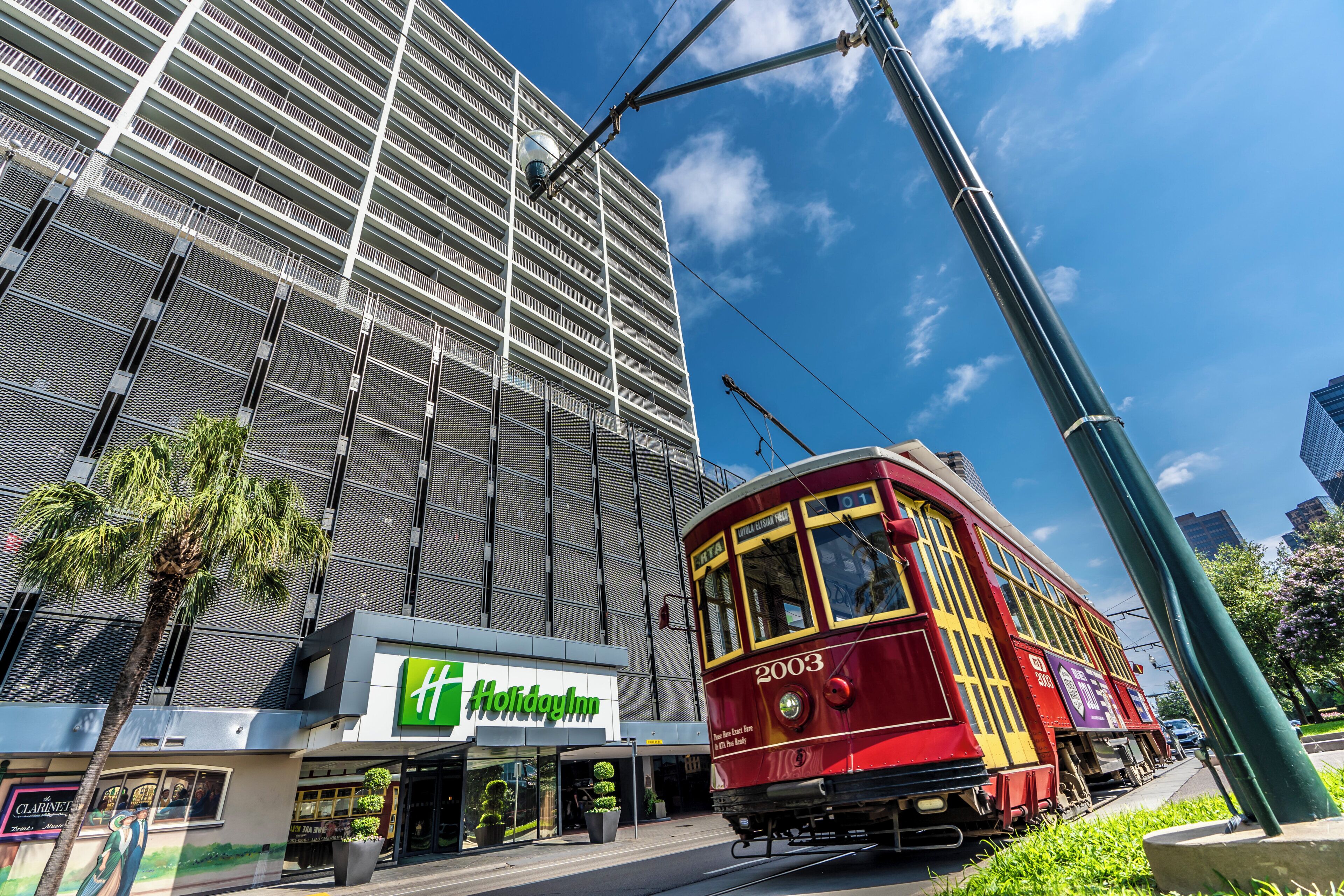 A red tram with the number 2003 passing by a Holiday Inn hotel with a modern building in the background.