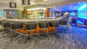 Zona de bar con una barra larga, varios taburetes y una amplia selección de botellas.