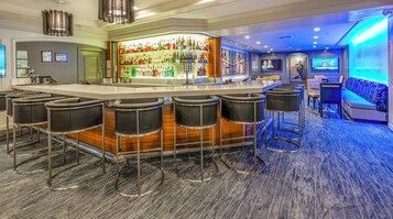 A bar area with a long counter, multiple stools, and a variety of bottles.