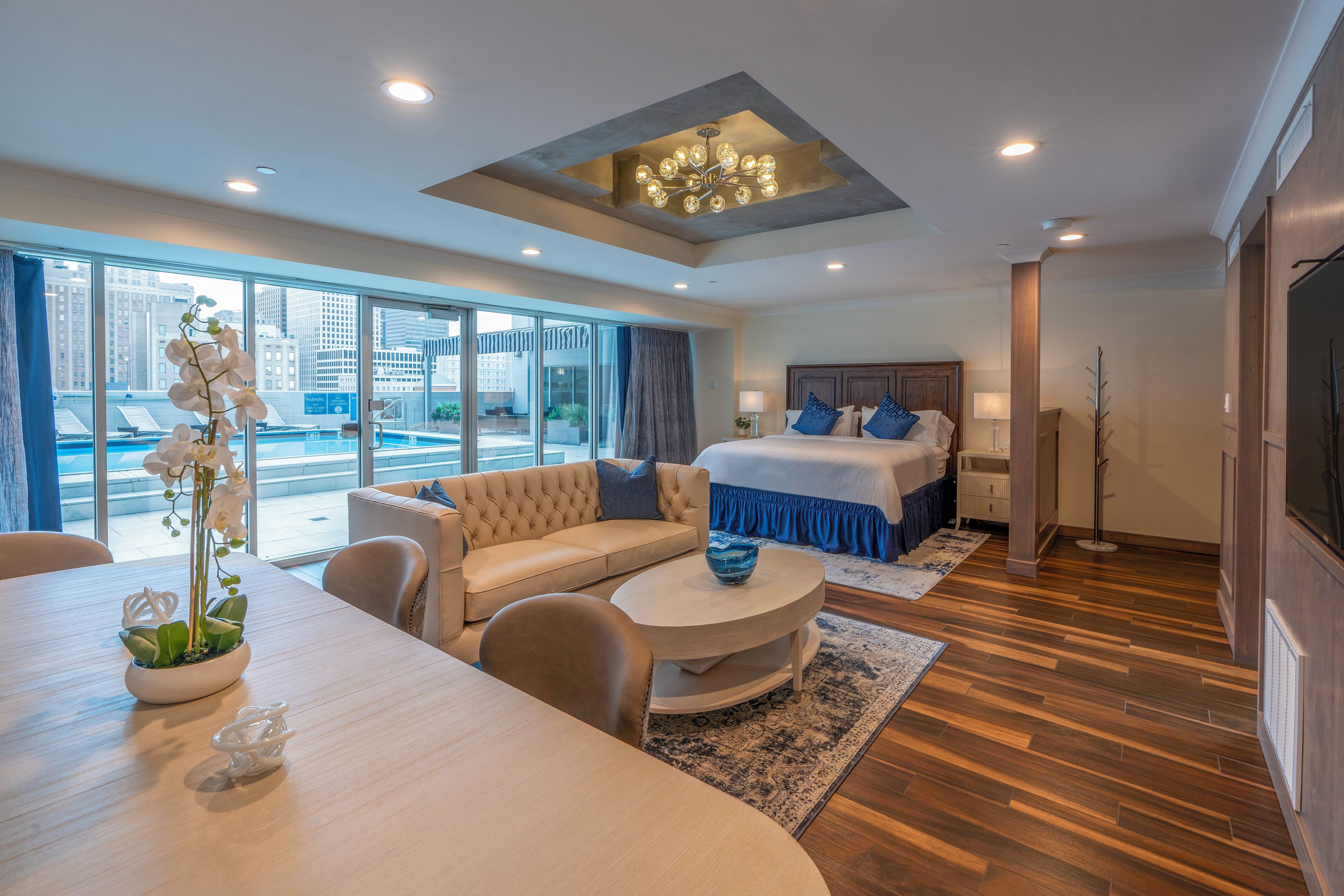 Habitaci ón de hotel moderna con una cama grande, un sofá, una mesa de comedor y vistas a la ciudad a través de amplias ventanas.