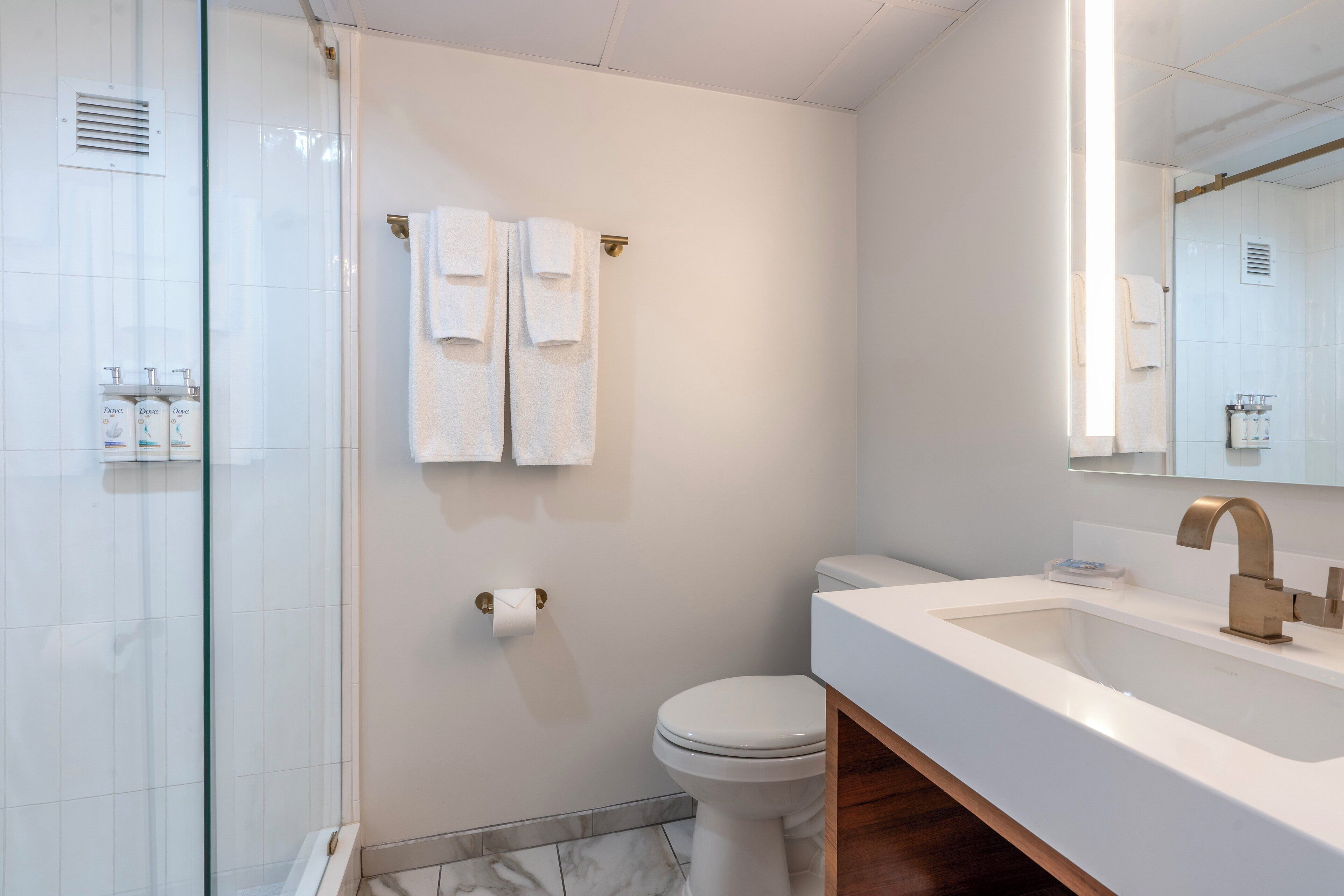 A modern bathroom with a glass shower enclosure, a toilet, a sink with a gold faucet, and a mirror above the sink.