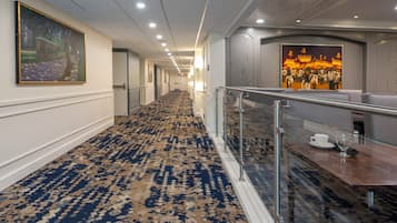 Un couloir d’hôtel avec un tapis à motifs, une rambarde en verre et des œuvres d’art accrochées aux murs.