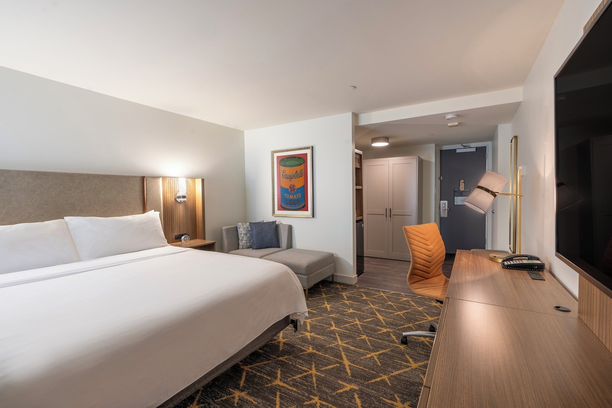 Una habitación de hotel con una cama grande, un escritorio, una silla, una lámpara y un televisor.