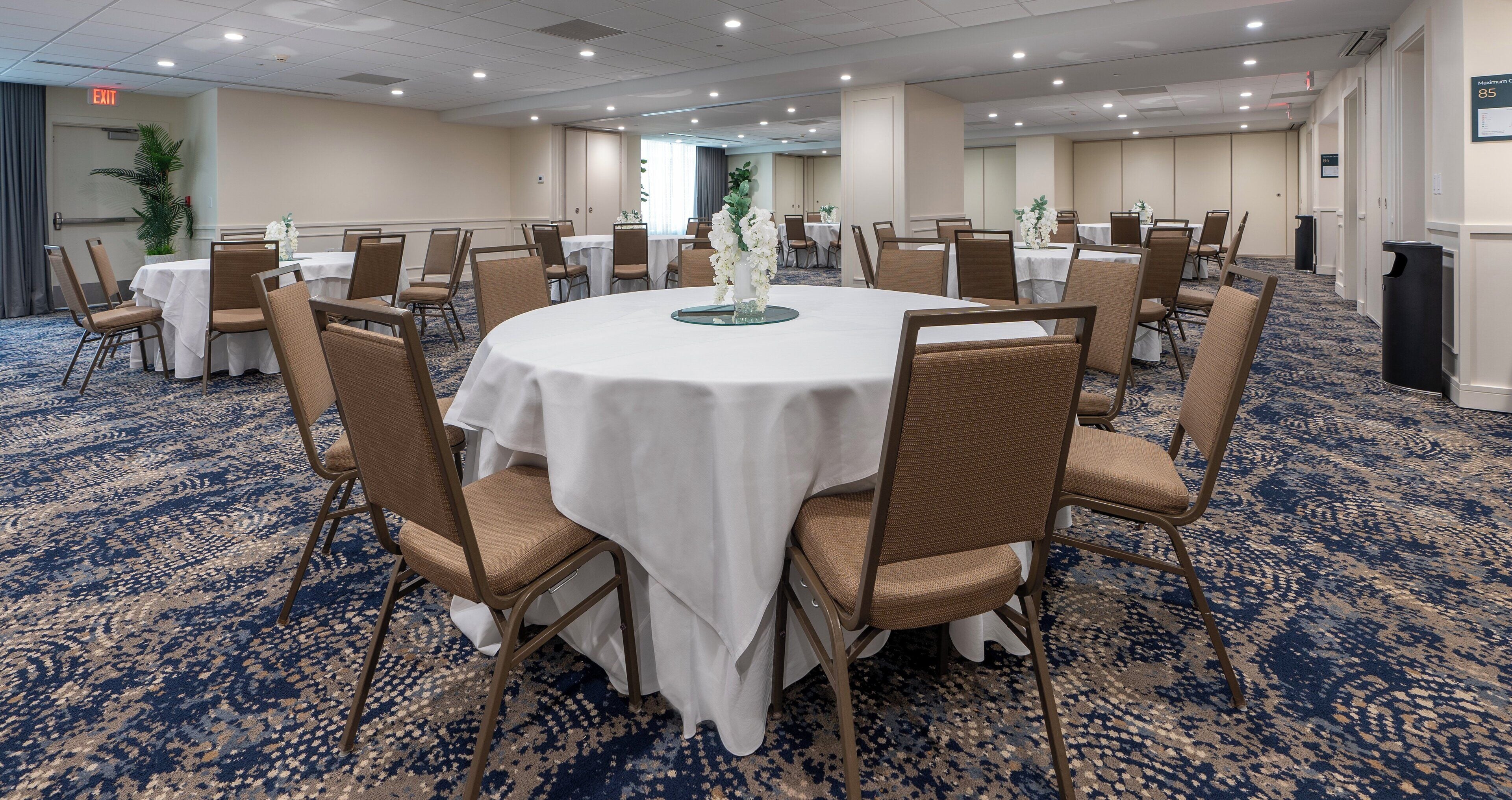 Un salón de conferencias con mesas redondas, sillas y suelo alfombrado.