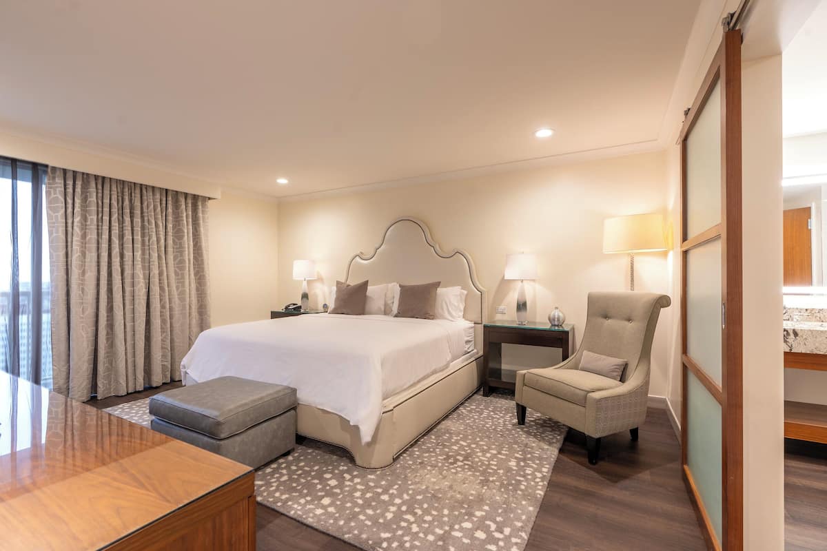 A hotel room with a large bed, a desk, a chair, and a nightstand.