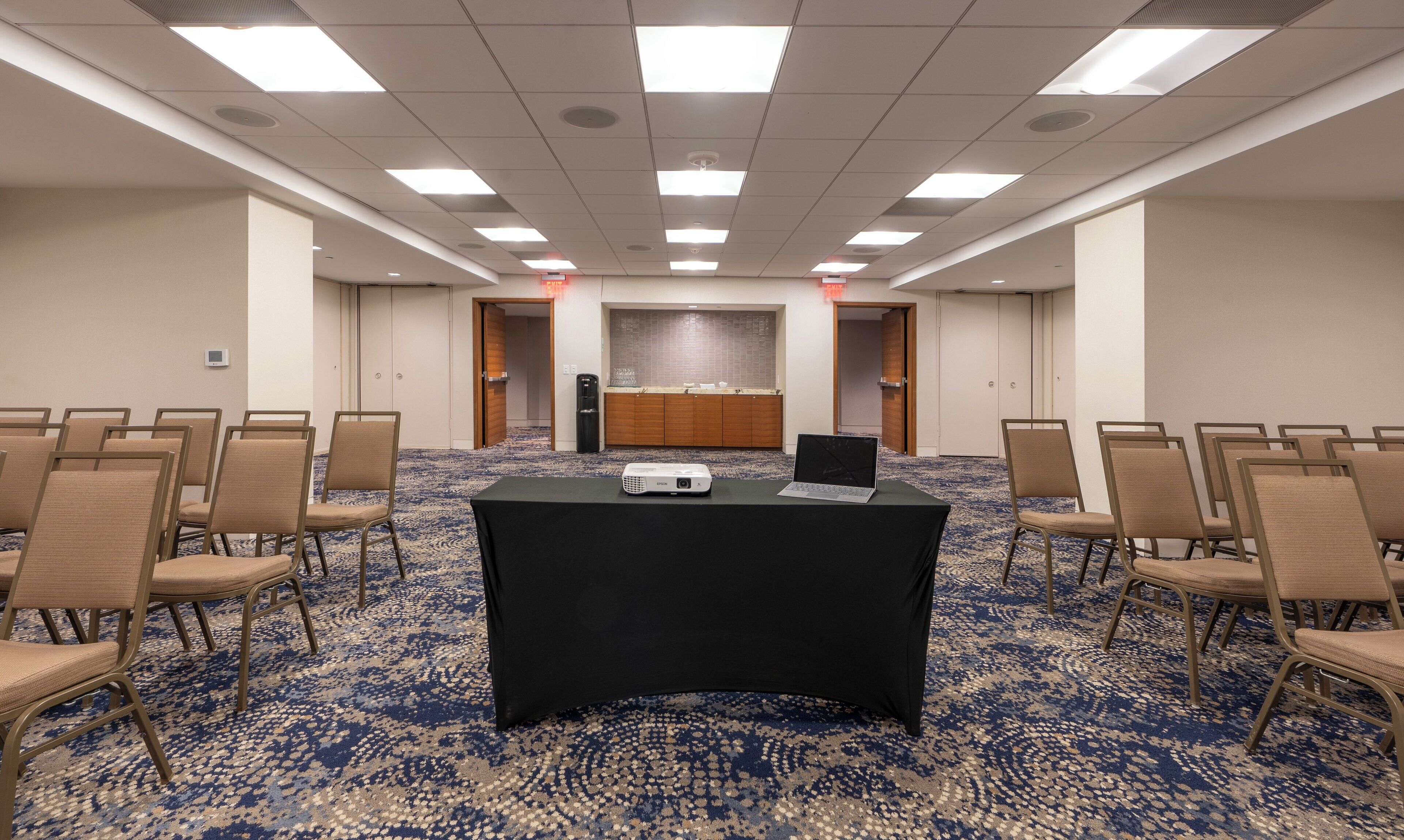 A conference room with a black table, chairs, a projector, and a tiled backsplash.