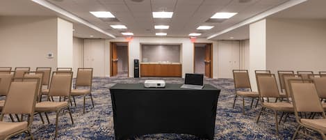 A conference room with a black table, chairs, a projector, and a tiled backsplash.