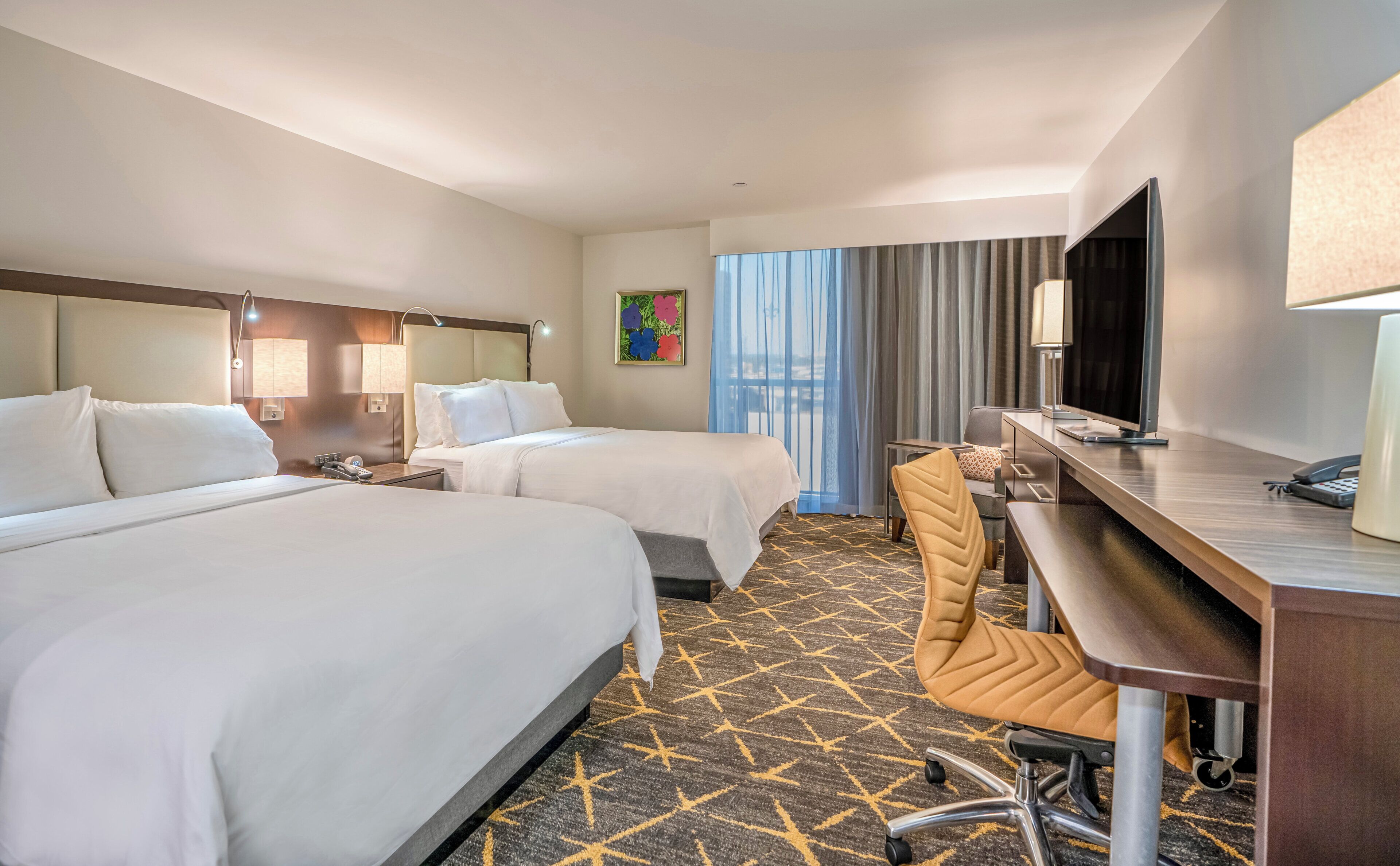A hotel room with two beds, a desk with a chair, a television, and a window with curtains.