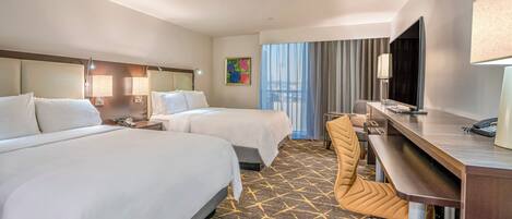 A hotel room with two beds, a desk with a chair, a television, and a window with curtains.