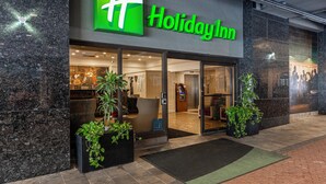 Exterior de un hotel Holiday Inn con un logotipo verde llamativo, puertas de cristal grandes y plantas en macetas en la entrada.
